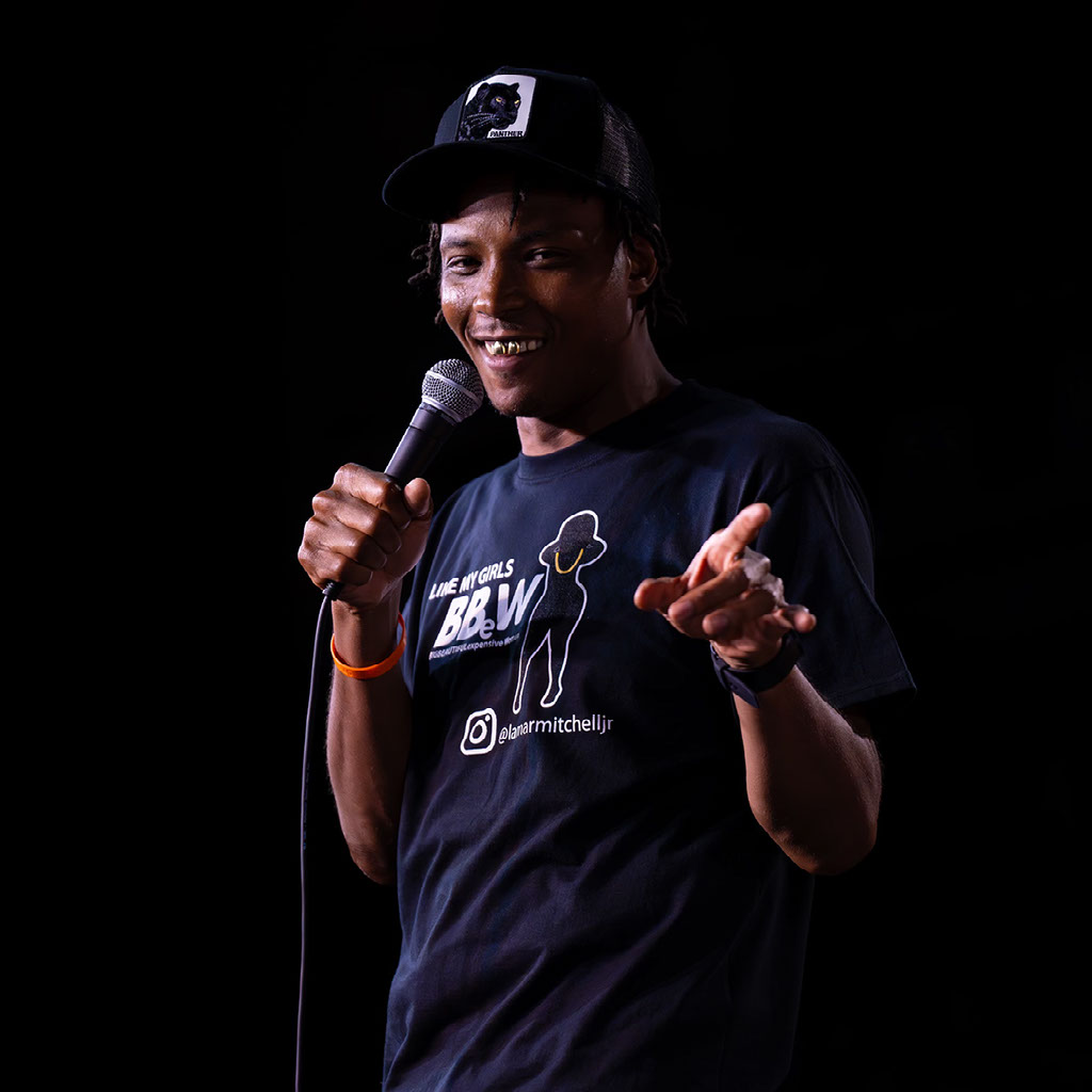 Lamar Mitchell J.R. smiling and holding a microphone in a branded T-shirt.